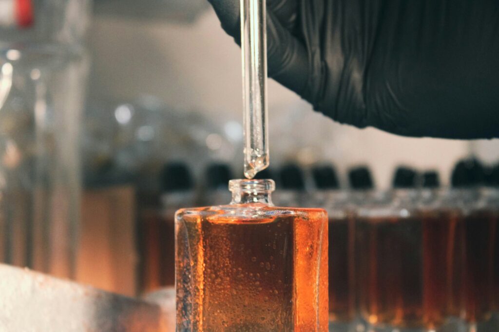 Gloved hand filling glass bottle with amber liquid using a dropper.